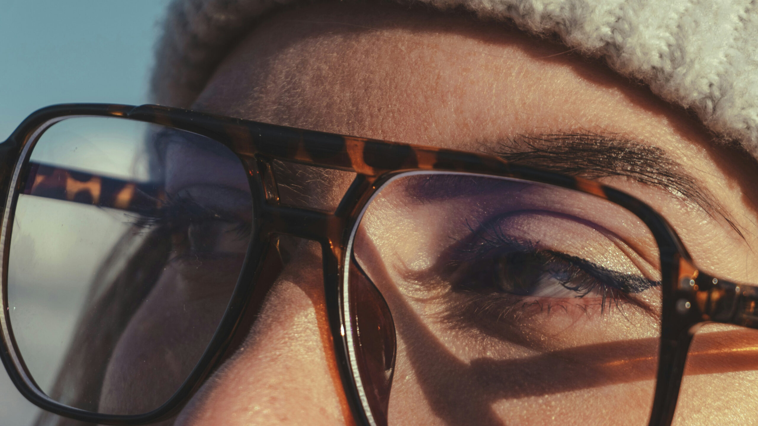 polina-kuzovkova-aM1amJ424IA-unsplash Close-up of a person wearing tortoiseshell glasses and a knit hat in sunlight