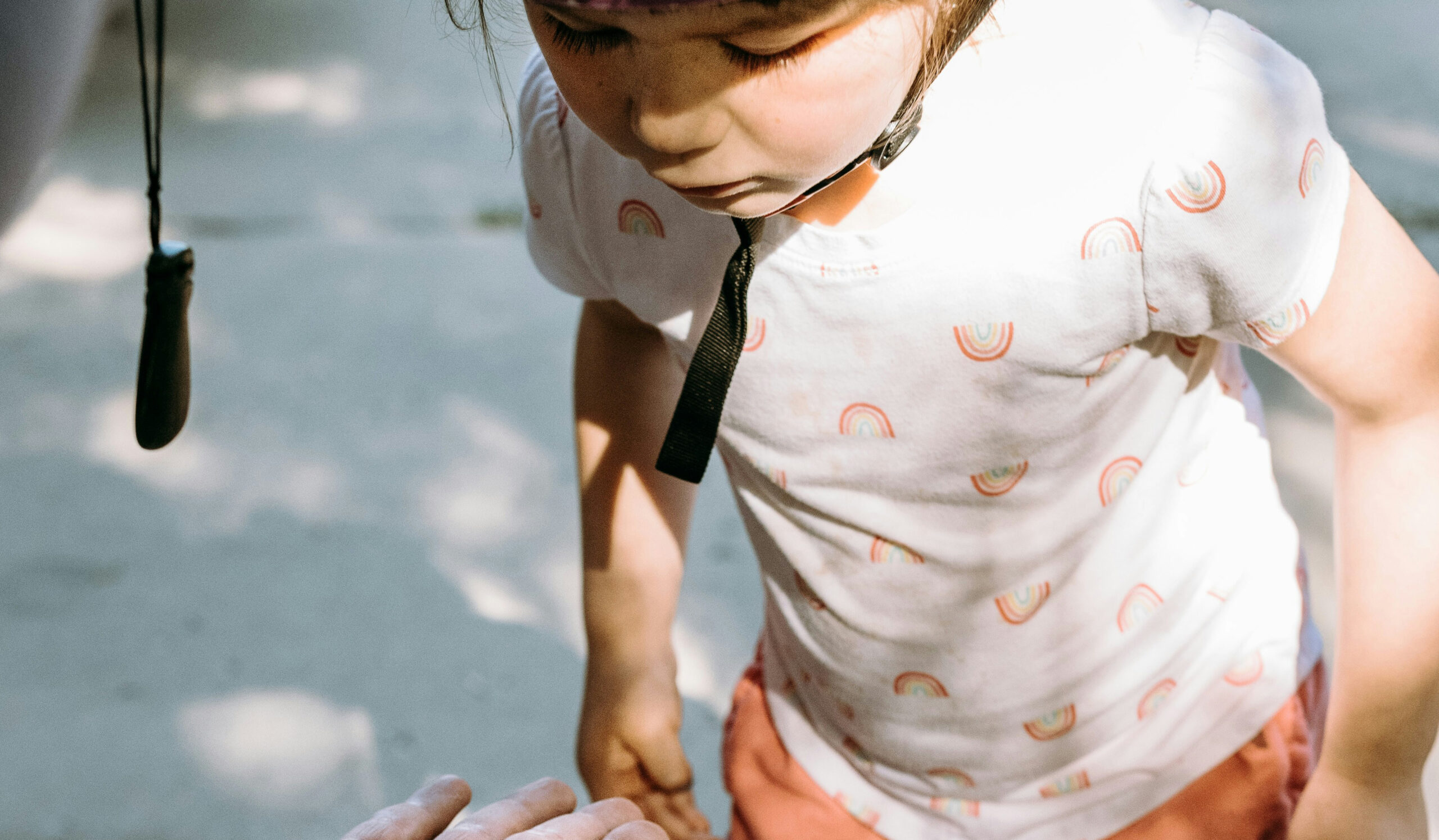 Young child looking down at an adult’s open hand in natural sunlight
